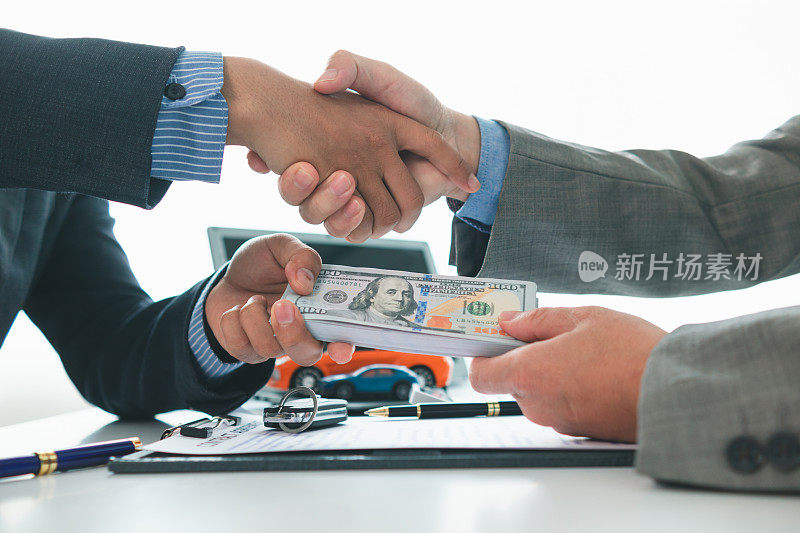 客户与汽车经销商在签订销售合同后握手，然后支付合同款项并将车钥匙交给客户。客户和汽车经销商之间握手的概念。