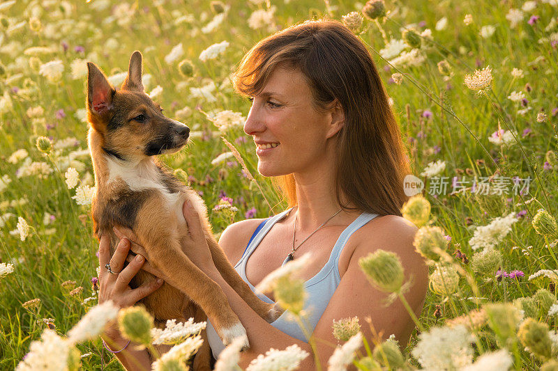 肖像，DOF:快乐的狗主人抱着她的小狗，他们坐在草地上
