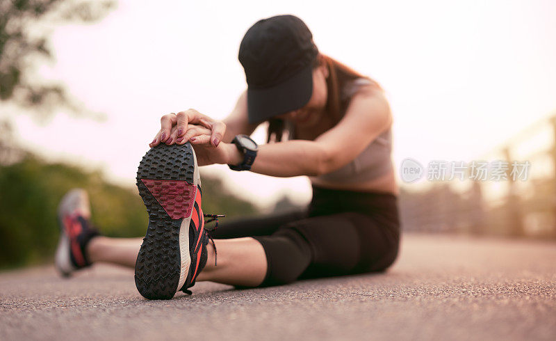 女运动员在慢跑前做伸展运动，女人在日落时伸展腿。