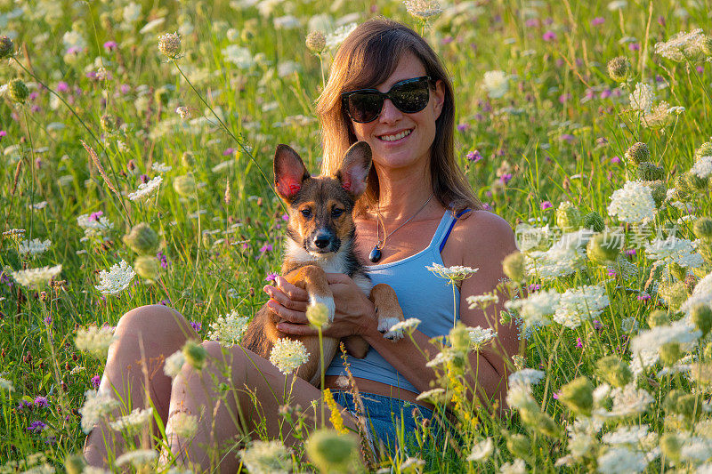 肖像，DOF:一个戴着太阳镜的微笑女人拥抱着她可爱的小狗