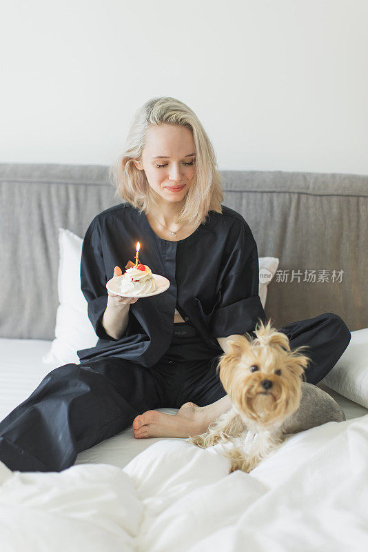 床上有蛋糕的金发女郎。庆祝生日。小的狗。约克郡犬