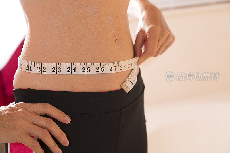 健康生活方式:注重体重的女性用卷尺测量腰围。