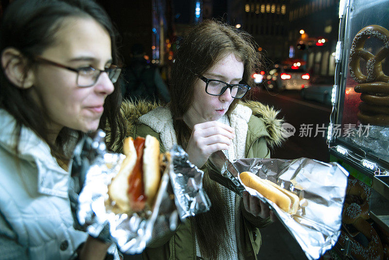 两个十几岁的女孩，姐妹，在街上吃快餐