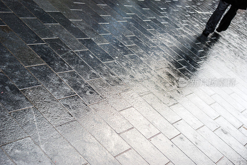 一个男人走在潮湿的人行道上的影子和腿