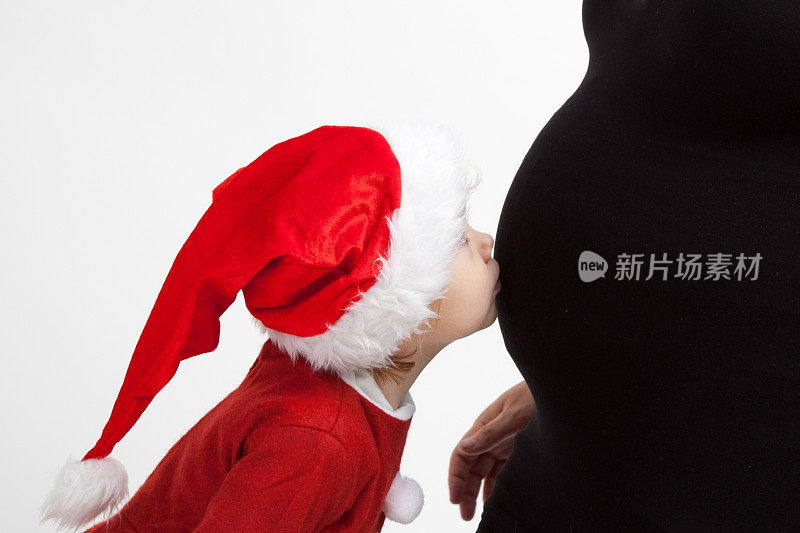 年轻女孩戴着圣诞帽，亲吻妈妈怀孕的肚子