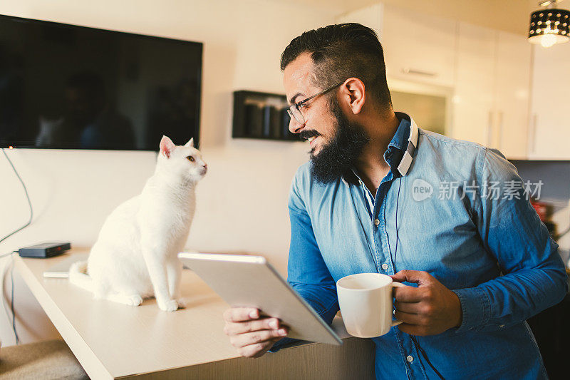 一名男子在家里使用数码平板电脑，旁边还有一只猫
