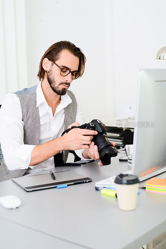 男性摄影师在办公室用电脑、相机和平板电脑编辑摄影