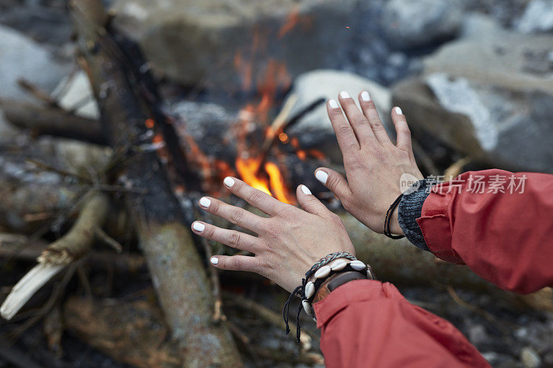 年轻女子在炉火旁取暖。近距离观察双手