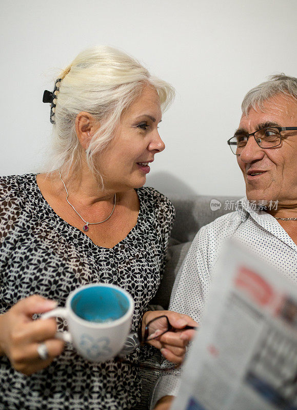在客厅的沙发上放着一对快乐的夫妇和报纸的肖像