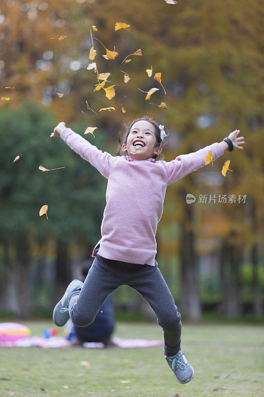 快乐的女孩在绿色的草地上跳跃。
