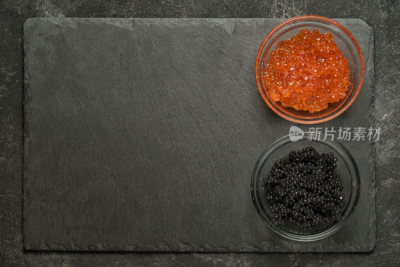 红色鲑鱼和黑色鲟鱼鱼子酱在一边的黑色石头板上的黑色桌子，顶视图与拷贝空间。
