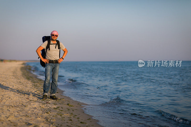 一个双手叉腰，面带微笑的男人站在海边