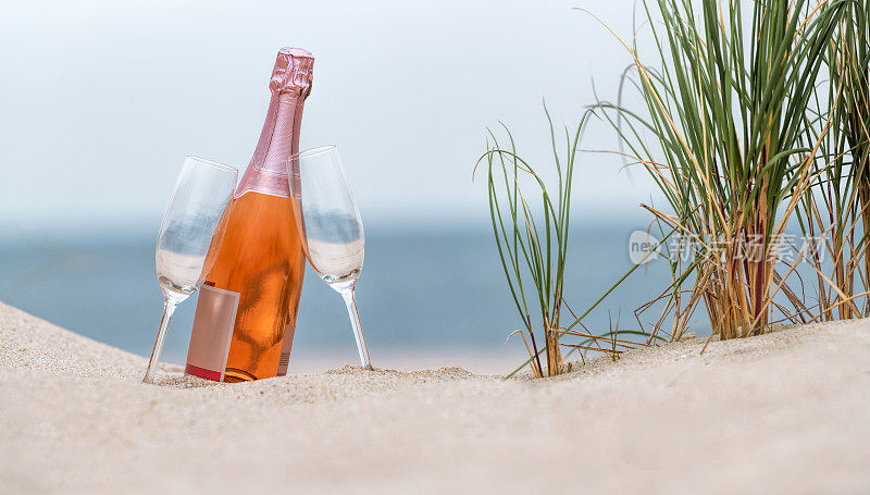 在沙滩上的沙滩上，两个酒杯和一瓶玫瑰香槟