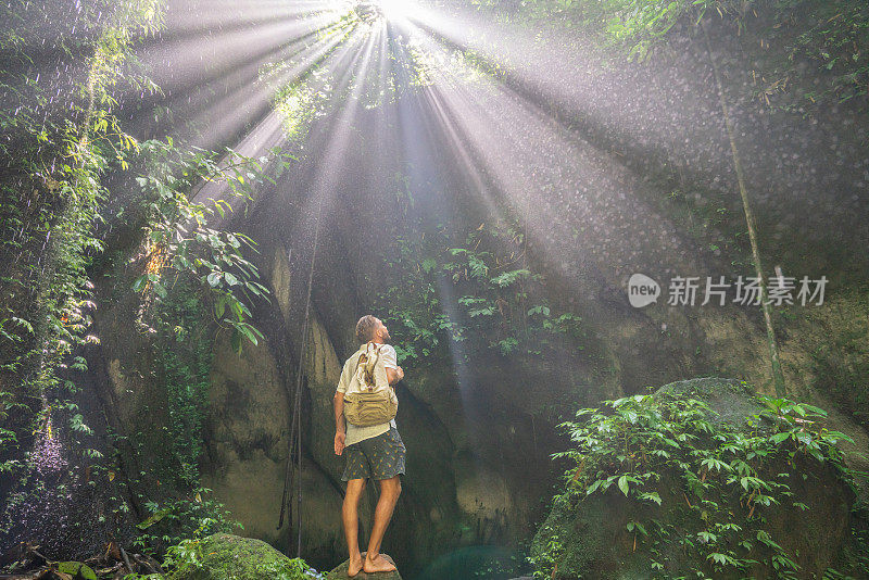 旅人站在热带雨林的洞穴里，仰望着从岩石上射下来的壮丽的阳光。人们旅行的奇妙欲望自然的概念
