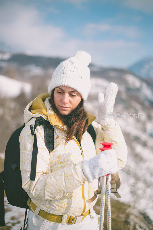 近景美丽的年轻女子在冬天的衣服站在一边，手拿木棍的背景雪山