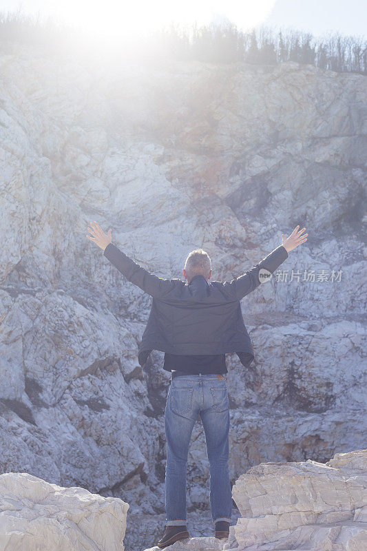 成年男子站在一些废弃的大理石采石场，手臂举起，伸开