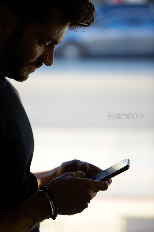 男人站在窗边用手机发短信的剪影