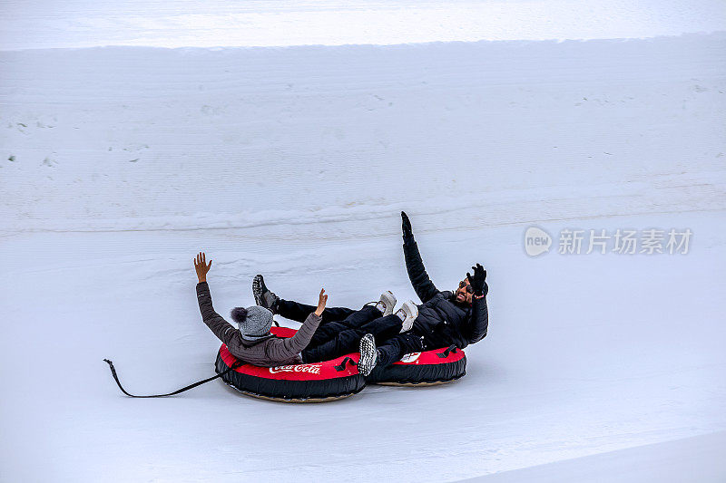 在科罗拉多州温特公园，一对夫妇在油管雪橇上从山上滑下来