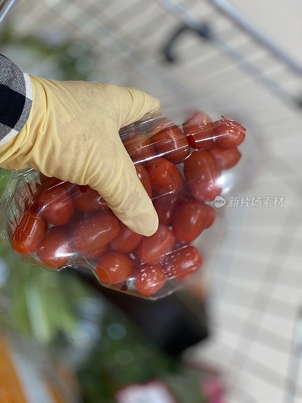 特写一只手与保护手套拿着一盒新鲜的红色樱桃番茄