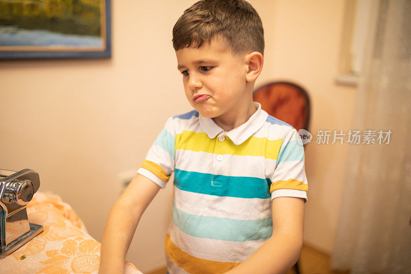 一个男孩在意大利面机旁边做鬼脸