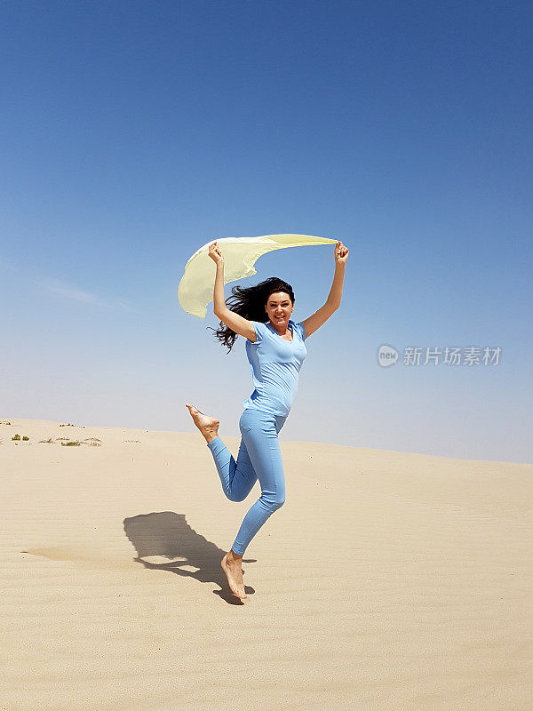 一个年轻女子在沙漠的沙子上跳。