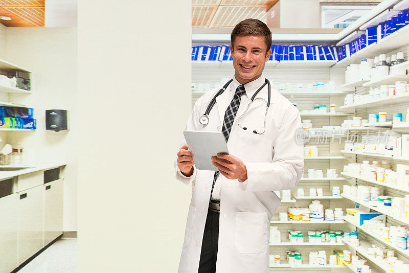 白人男医生穿着实验服，用着平板电脑站在商店的商品前