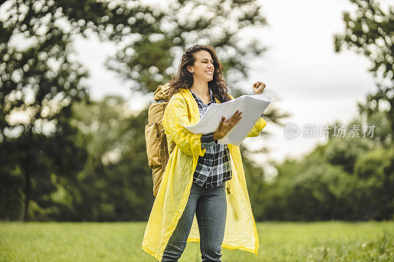 年轻女子穿着防水夹克，看地图，在雨中徒步旅行