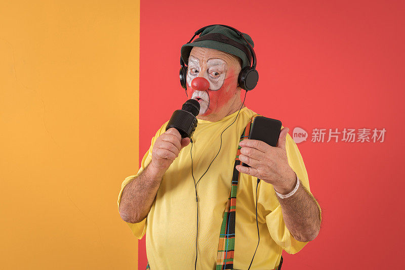 滑稽的老年小丑在彩色背景前用麦克风唱着歌