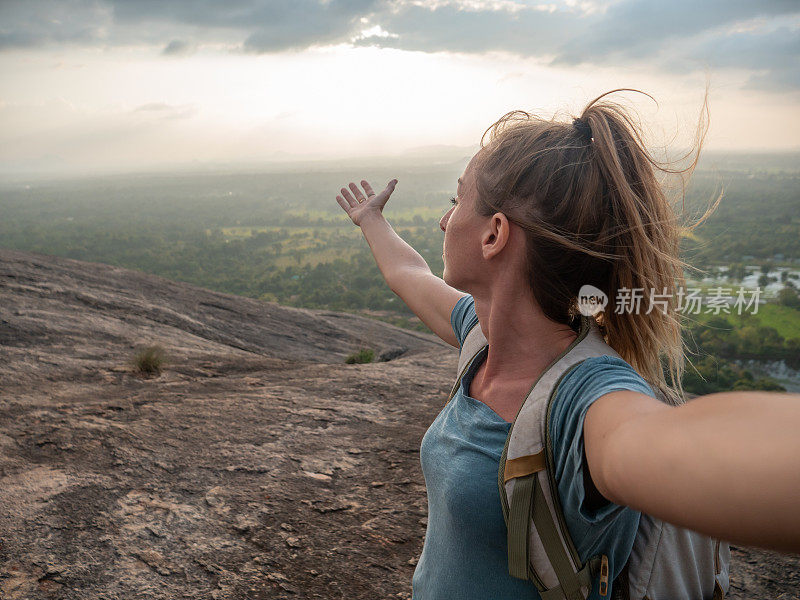 年轻女子在岩石上张开双臂拥抱夕阳