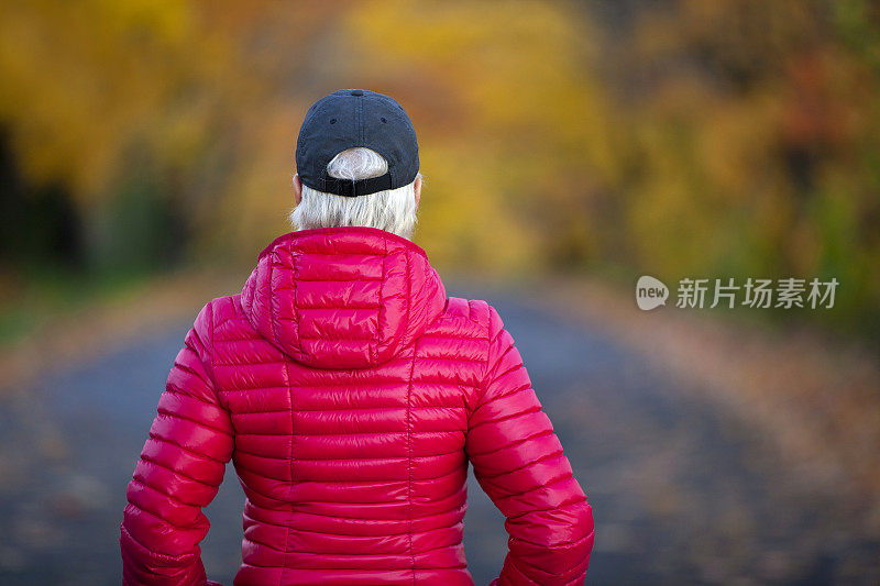 一个女人在路上看着秋天的树叶。