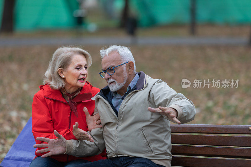 英俊的老男人和他的妻子坐在城市公园的长椅上进行严肃的讨论。