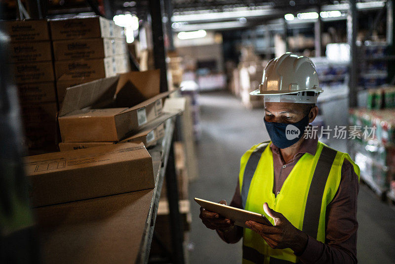 仓库工人戴口罩和防护服，用数码板检查产品