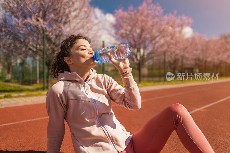 运动的年轻女子在运动轨道上跑步后喝水。