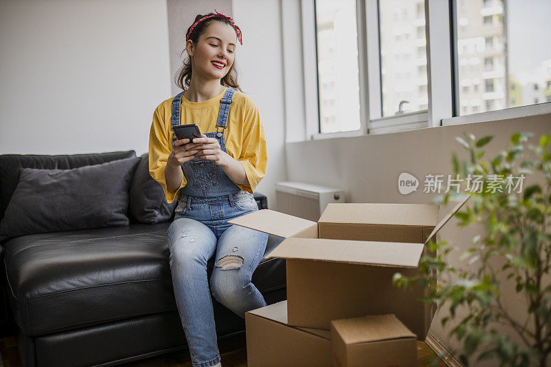 快乐的女人用电话和搬到新房子用纸板箱