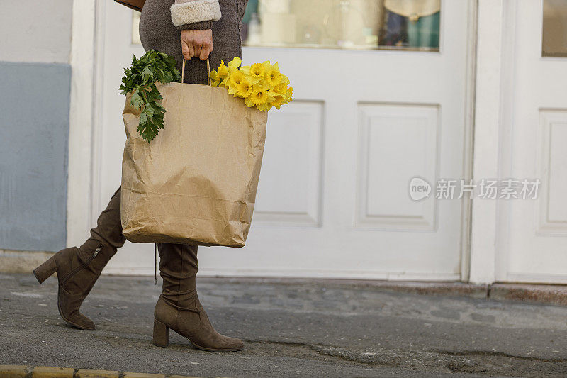 一个女人提着一个纸袋，走在城市的街道上