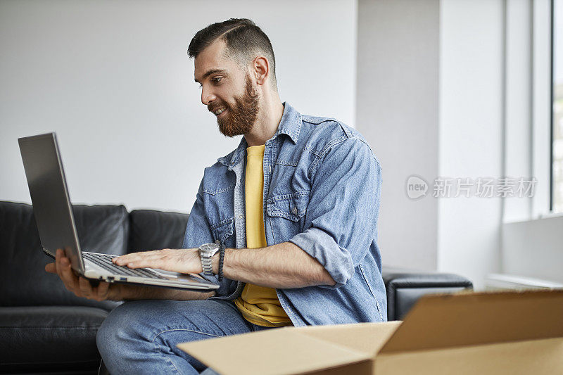 一个人在用他的笔记本电脑，坐在地板上，周围是移动的箱子。