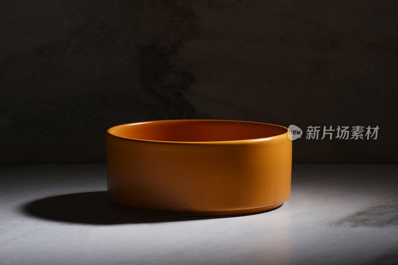 大理石背景上的橙色空陶瓷碗