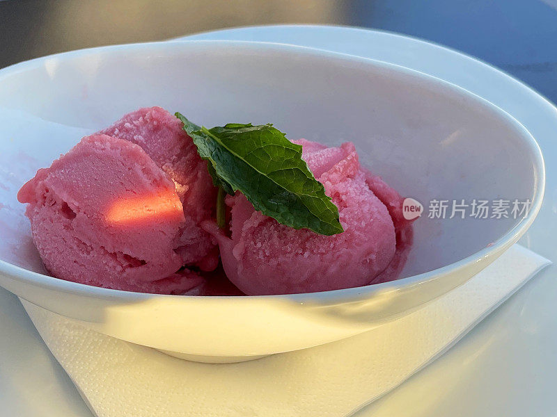 图片中的草莓和覆盆子冰沙餐厅甜点勺薄荷叶装饰在白色的碗，聚焦前景