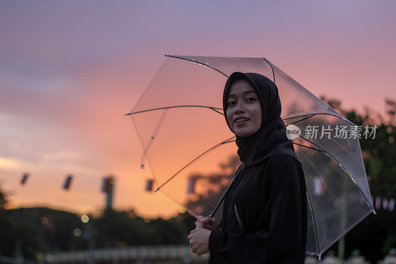 日落时分，亚洲妇女撑着伞站在城市公园里