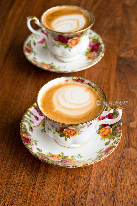 家庭咖啡师-自制的纯白咖啡和脱脂牛奶在一对古董骨瓷杯古董胡桃木桌子上