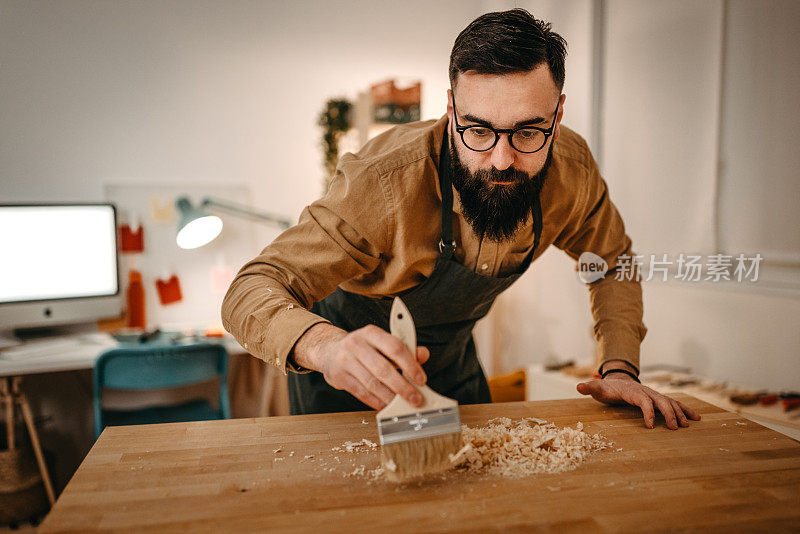 男艺术家在工作室工作台上清理木头上的灰尘