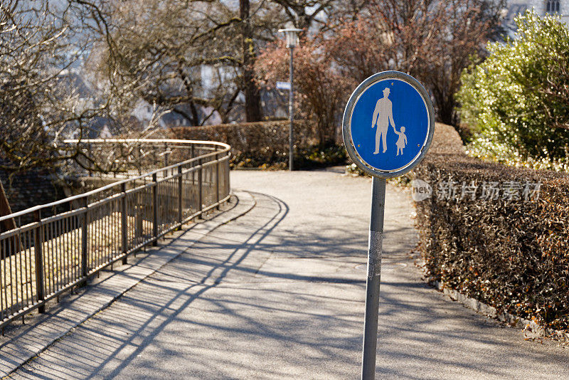 蓝色的人行道标志、交通标志、蓝色背景的白漆男人和小孩:行人和使用类车辆设备的人必须使用该路径。背景有栏杆的混凝土路径