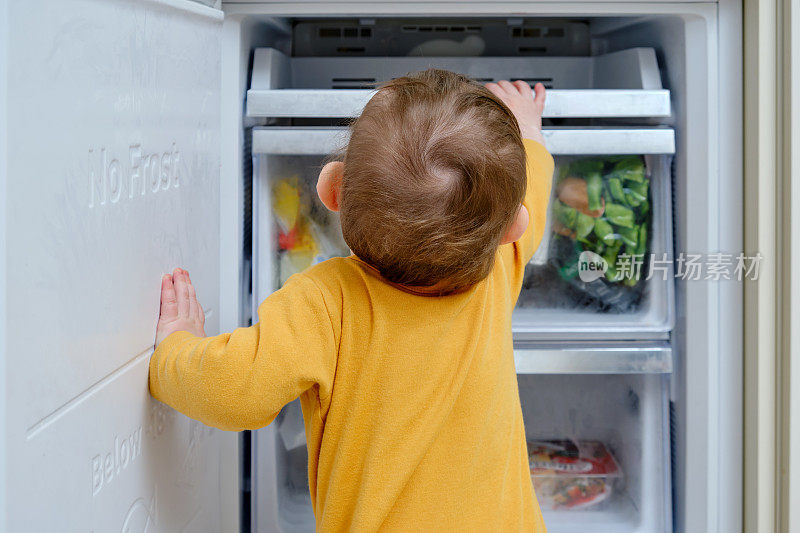 蹒跚学步的小男孩往打开的冰箱里看。孩子的安全问题，孩子的安全问题，孩子的安全问题
