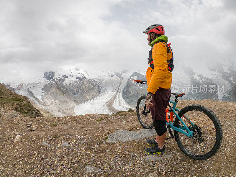 男性山地自行车爱好者欣赏风景，土路，远处的冰川
