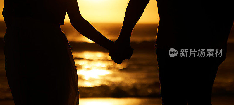 夕阳西下沙滩上手牵手的情侣。一对夫妇在海边散步度假的特写镜头。沙滩上牵手的情侣剪影。一对夫妇在海滩上度假