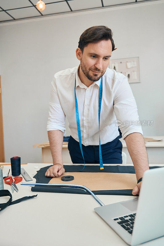 缝纫车间的服装设计师使用缝纫设备和笔记本电脑工作