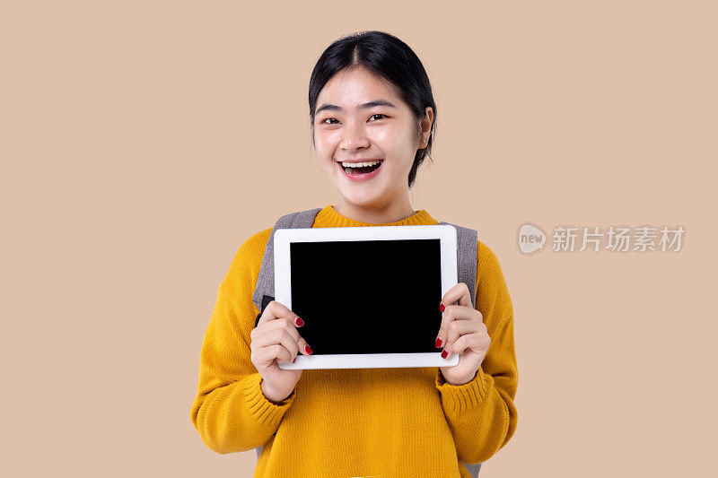 年轻的亚洲学生女孩拿着平板电脑与空白屏幕在孤立的背景