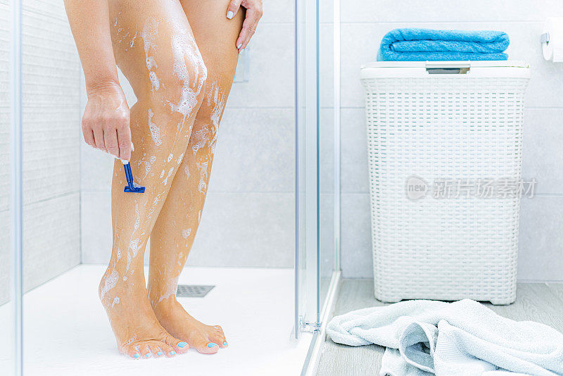 一个女人在淋浴间用剃刀刮腿毛