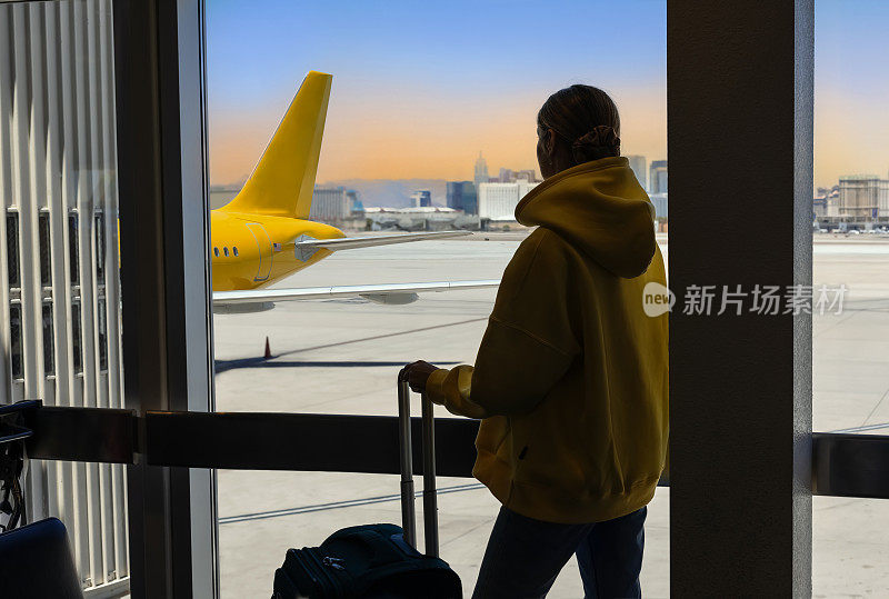 移民或移民概念。年轻女子带着随身行李悲伤地看着窗外的飞机在机场。