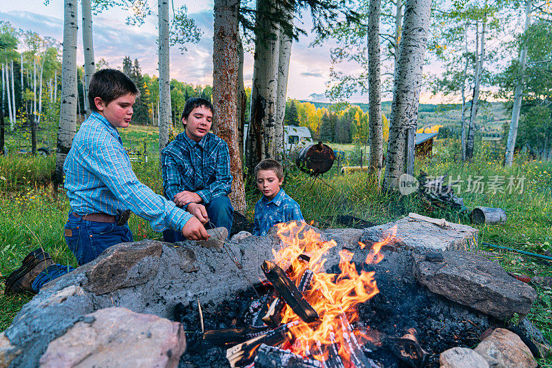 年轻的白人牧场主兄弟坐在一起，在美国科罗拉多州的一个小镇家庭拥有的农场后院的火坑里生火